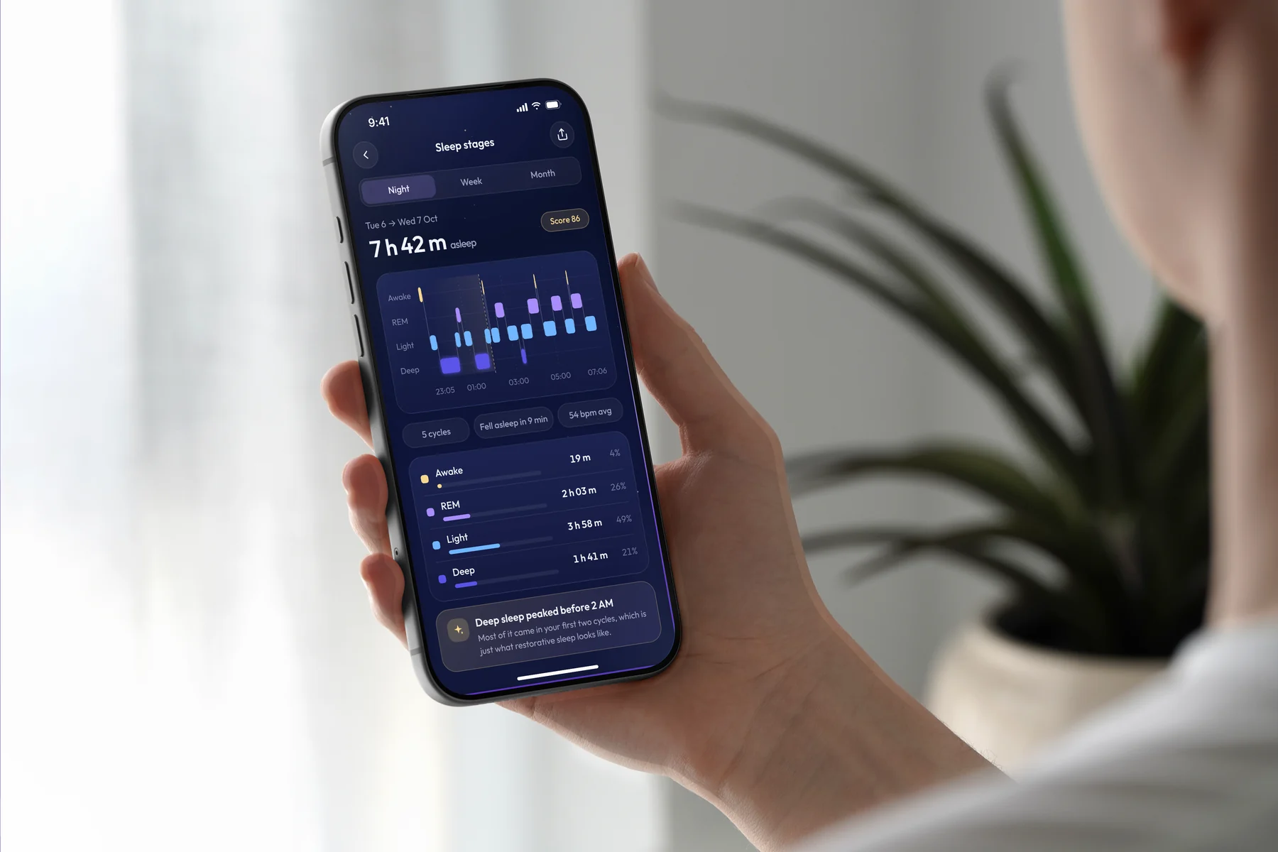 A real photo of a hand holding an iPhone 17 Pro at an angle, showing a sleep stages screen, with a plant in soft daylight behind